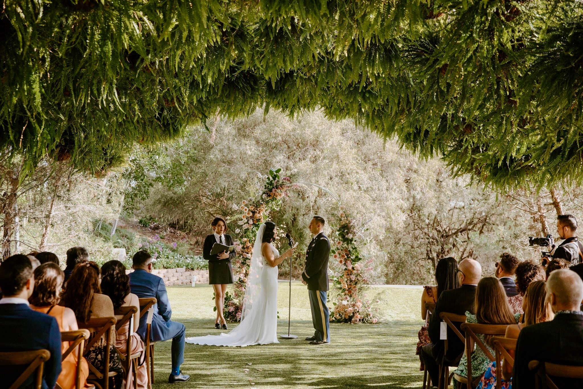 Outdoor Southern California wedding ceremony beneath a canopy of greenery, officiated by Priscilla Brehme